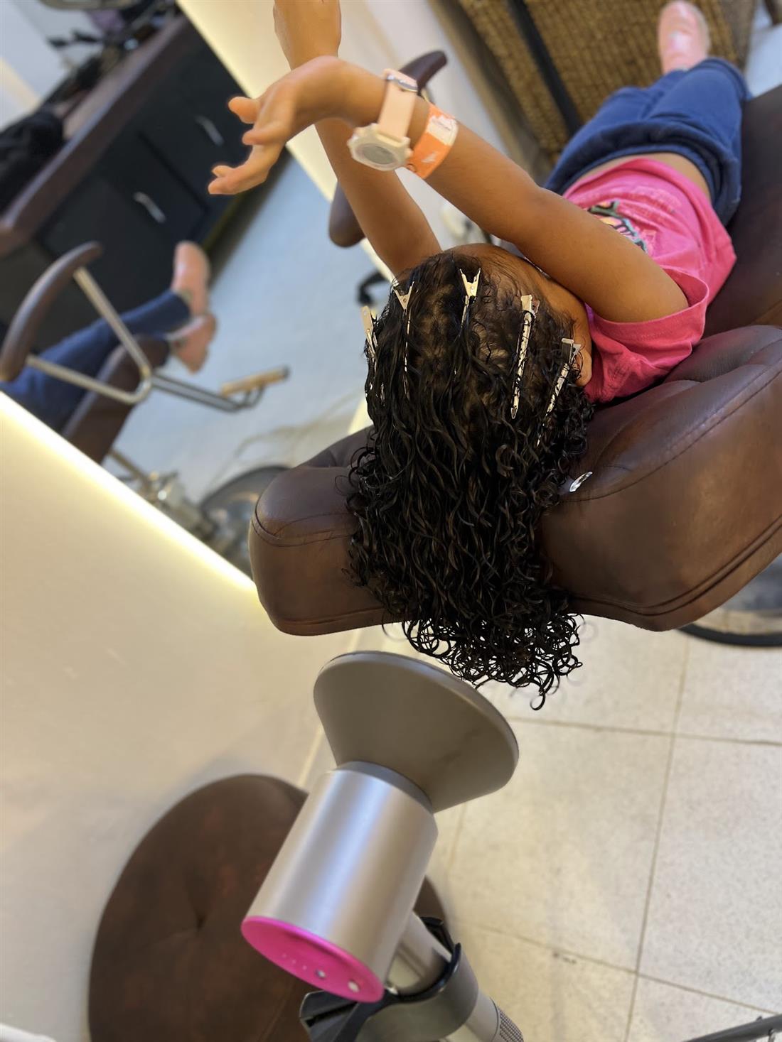 Niña con trenzas y rizos secándose con difusor en el salón